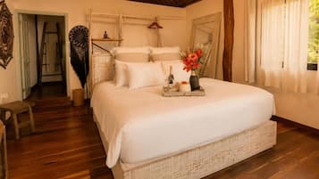Quarto espaçoso com uma cama grande, piso de madeira e teto de palha.