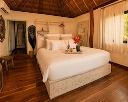 A spacious bedroom with a large bed, wooden flooring, and a thatched ceiling.