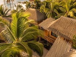 Un resort tropical con cabañas de techo de paja, palmeras y vista a la playa.