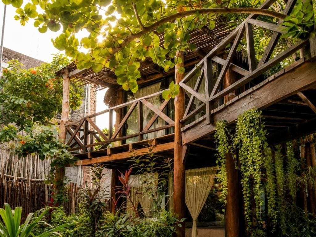 Una estructura de madera con techo, rodeada de abundante follaje y plantas.
