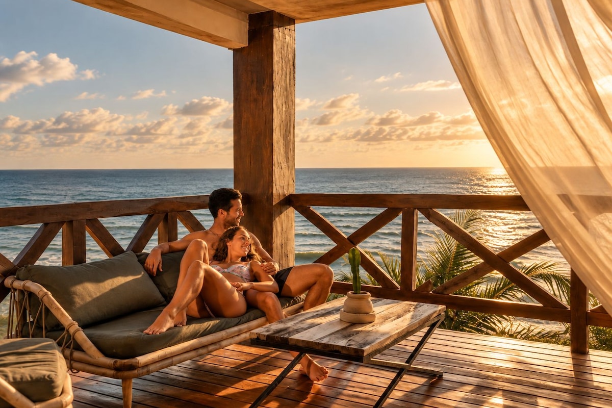 A wooden deck with a couple relaxing on a cushioned bench, overlooking the ocean.