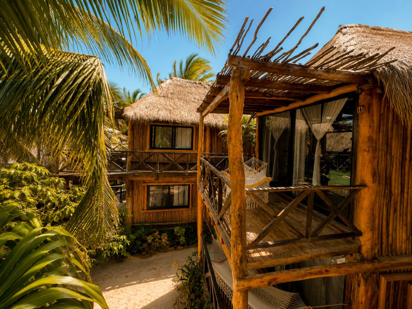 Une structure en bois avec un toit de chaume, un balcon et un espace salon abrité.