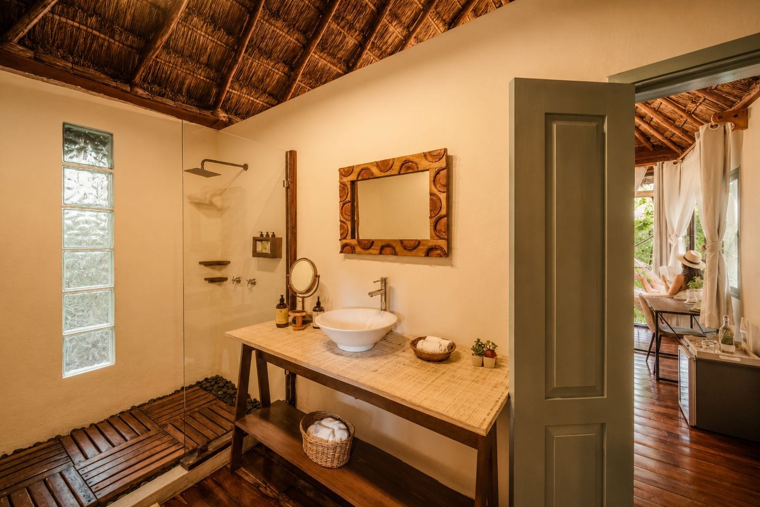 Un baño con banco de madera, espejo grande, lavabo y ducha.