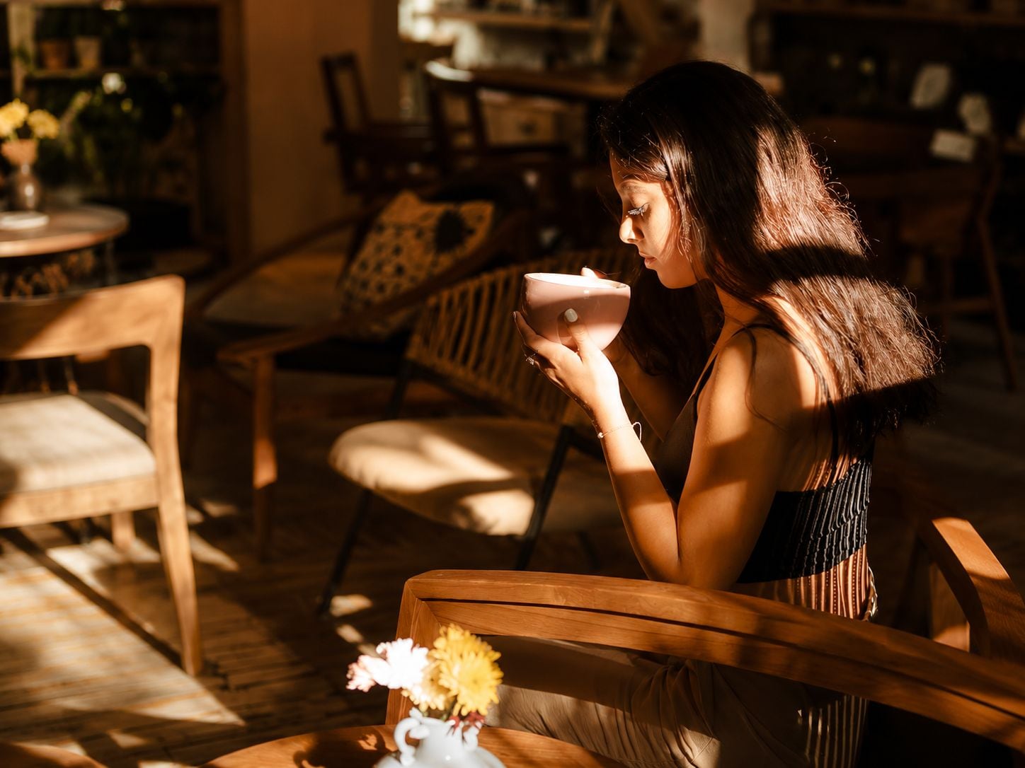 A person sitting on a wooden chair in a room with a table and a vase of flowers.