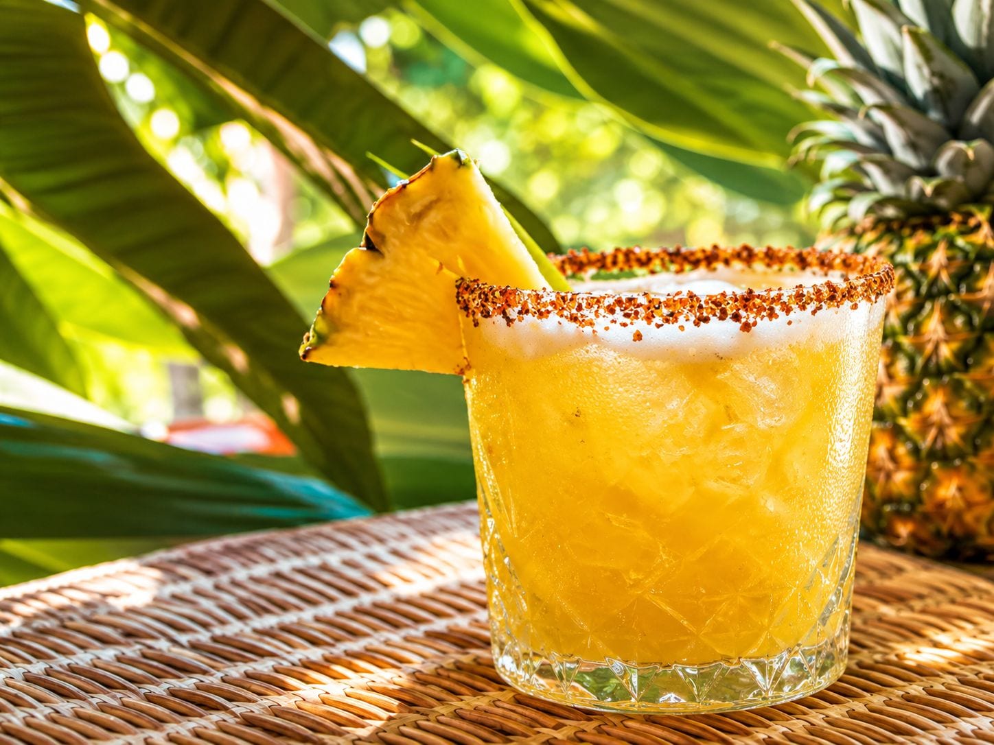 Un vaso con borde salado y una rodaja de piña, sobre una superficie tejida.