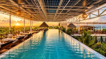 An infinity pool with lounge chairs and a view of the ocean at sunset.