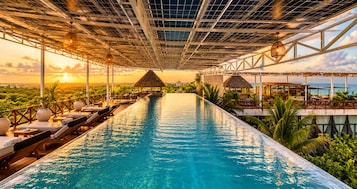 An infinity pool with lounge chairs and a view of the ocean at sunset.