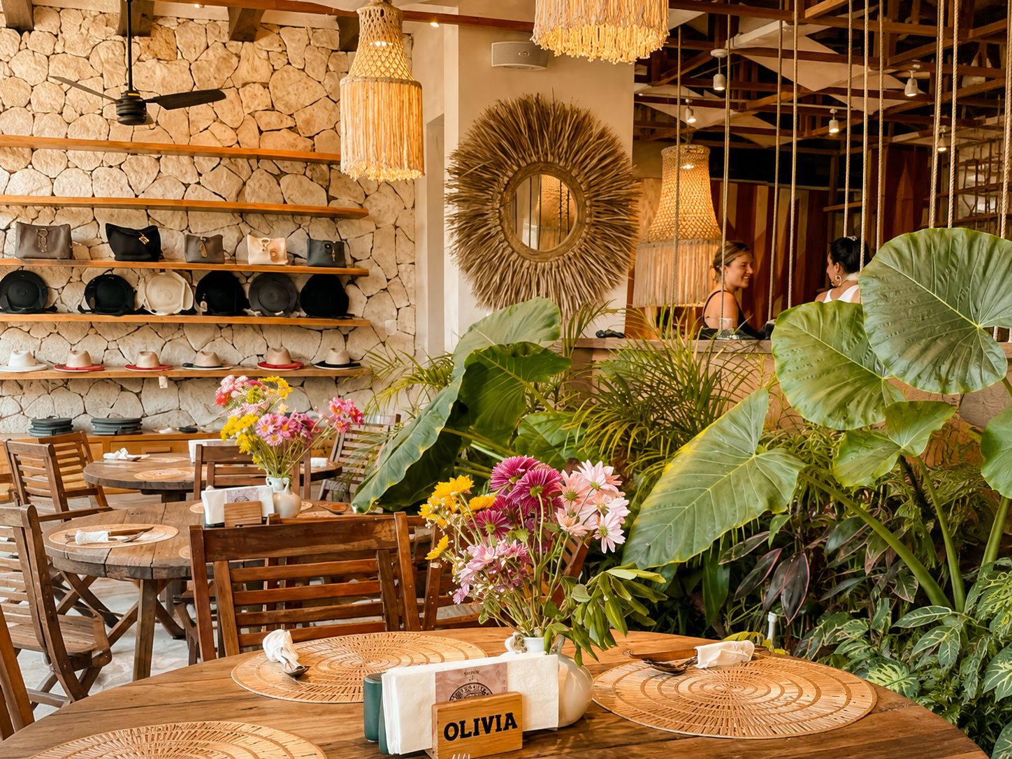A restaurant interior with wooden tables, chairs, and a stone wall.