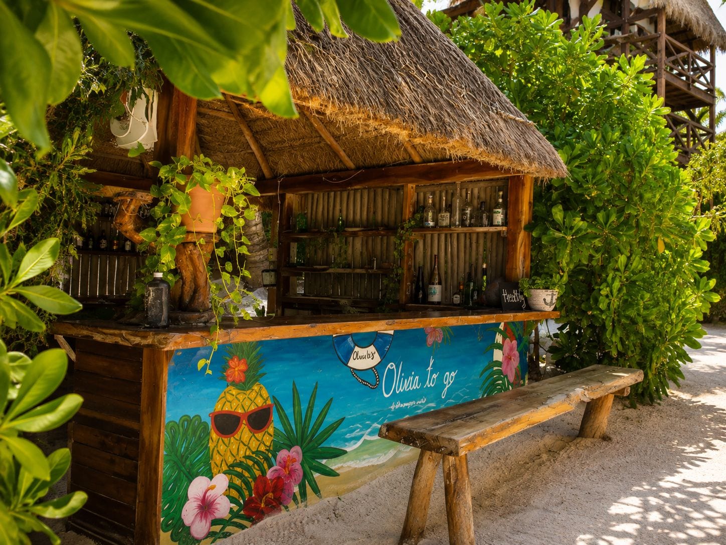 A tiki bar with a thatched roof, surrounded by tropical plants and a beach-themed mural.