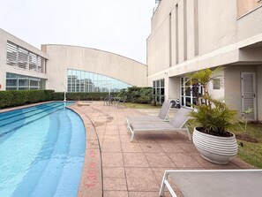 A swimming pool with lounge chairs and a large planter, surrounded by a building with a curved facade and large windows. - Vrbo Property (São Paulo)