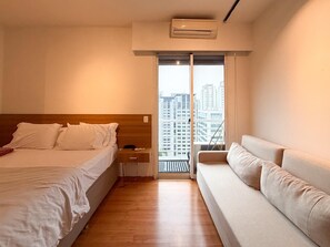 A hotel room with a bed, a sofa, a window with a view of buildings, and an air conditioning unit. - Vrbo Property (São Paulo)