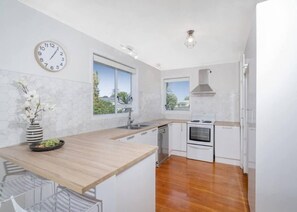 A modern kitchen with a wooden countertop, white cabinets, a built-in oven, and a clock on the wall.
