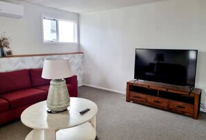 A living room with a red sofa, a round coffee table with a lamp, a wooden TV stand, and a large flat-screen TV.