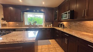 A kitchen with dark wood cabinets, a granite countertop, a built-in microwave, and a window with a view of greenery. - Song • Pinecrest Manor | Forest & Pond (Surrey)