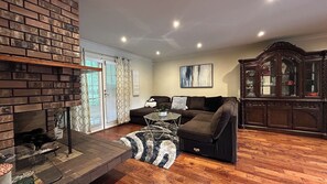 A living room with a fireplace, a sofa, a glass coffee table, and a cabinet. - Song • Pinecrest Manor | Forest & Pond (Surrey)