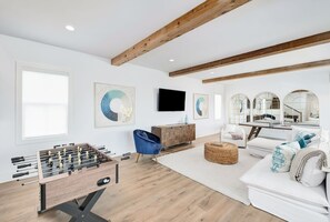 A spacious living room with a wooden ceiling, a foosball table, a blue armchair, a white sofa, and a large mirror. - Sleeps 26! Private Pool, Hot Tub, & Gulf Views! Walk 2 Beach! (Santa Rosa Beach)