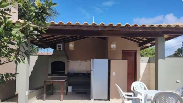 A covered outdoor area with a kitchen, a refrigerator, and a table with chairs. - Casa Brisa De Arraial (Porto Seguro)