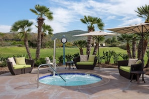 A hot tub surrounded by outdoor furniture, palm trees, and a clock.