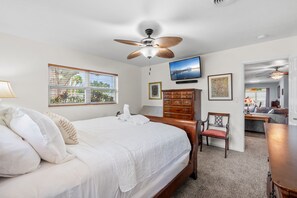 Une chambre à coucher comprenant un lit, une commode, une chaise, un téléviseur et un ventilateur de plafond.