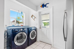 Una sala de bugaderia amb dues rentadores de càrrega frontal, un refrigerador i una finestra amb vista a l'exterior.