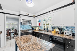 Una cocina moderna con encimeras de granito, armarios blancos y microondas integrado.