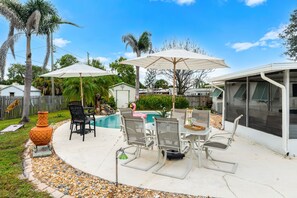 Un patio trasero con piscina, mobiliario exterior y sombrillas.