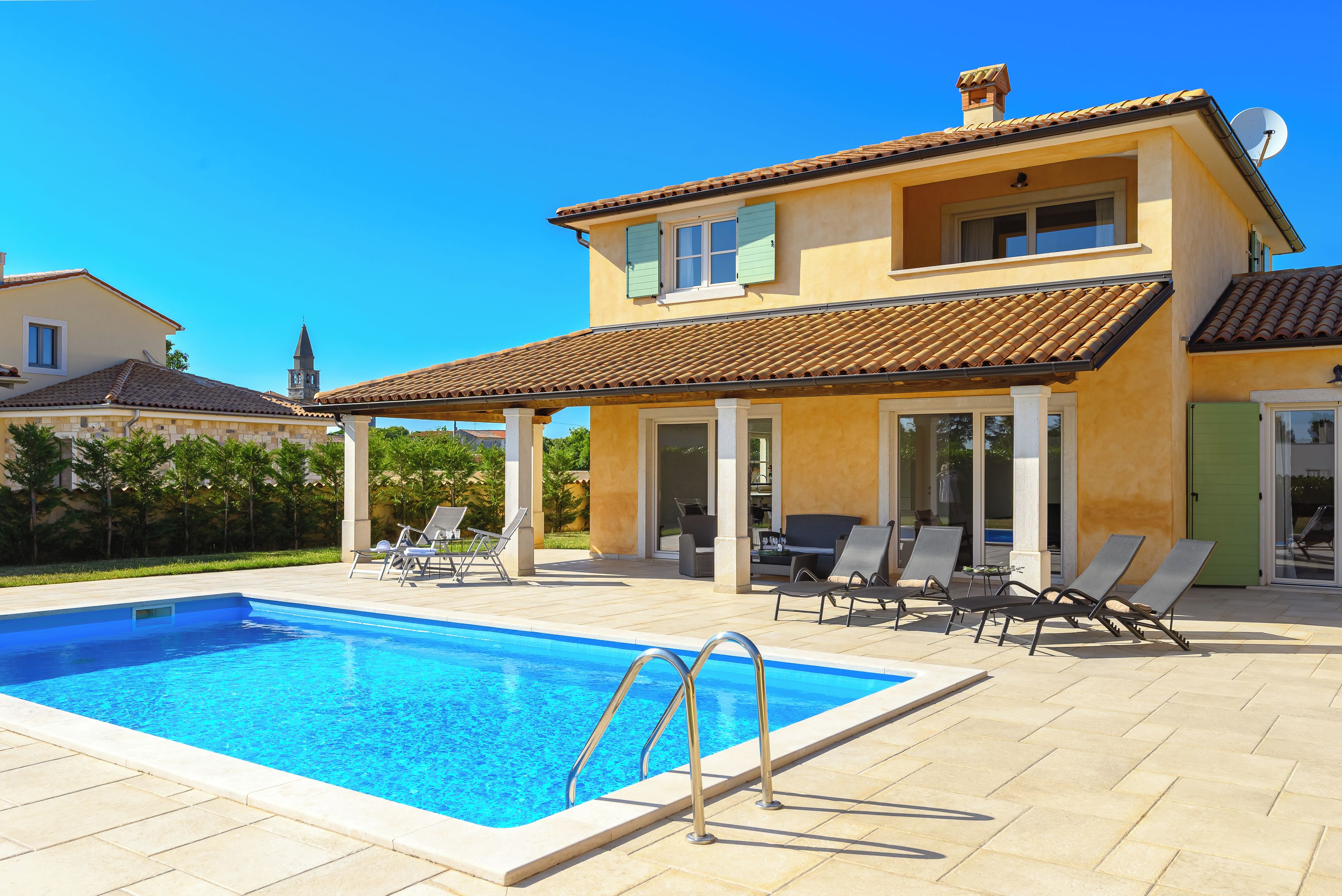 A two-story house with a swimming pool, outdoor seating, and a clear blue sky.