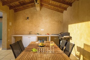 A wooden table with chairs, a bowl of fruit, and glasses of water in a kitchen area with wooden beams on the ceiling. - Villa Flori (Istria - Svetvinčenat) (Svetvinčenat)