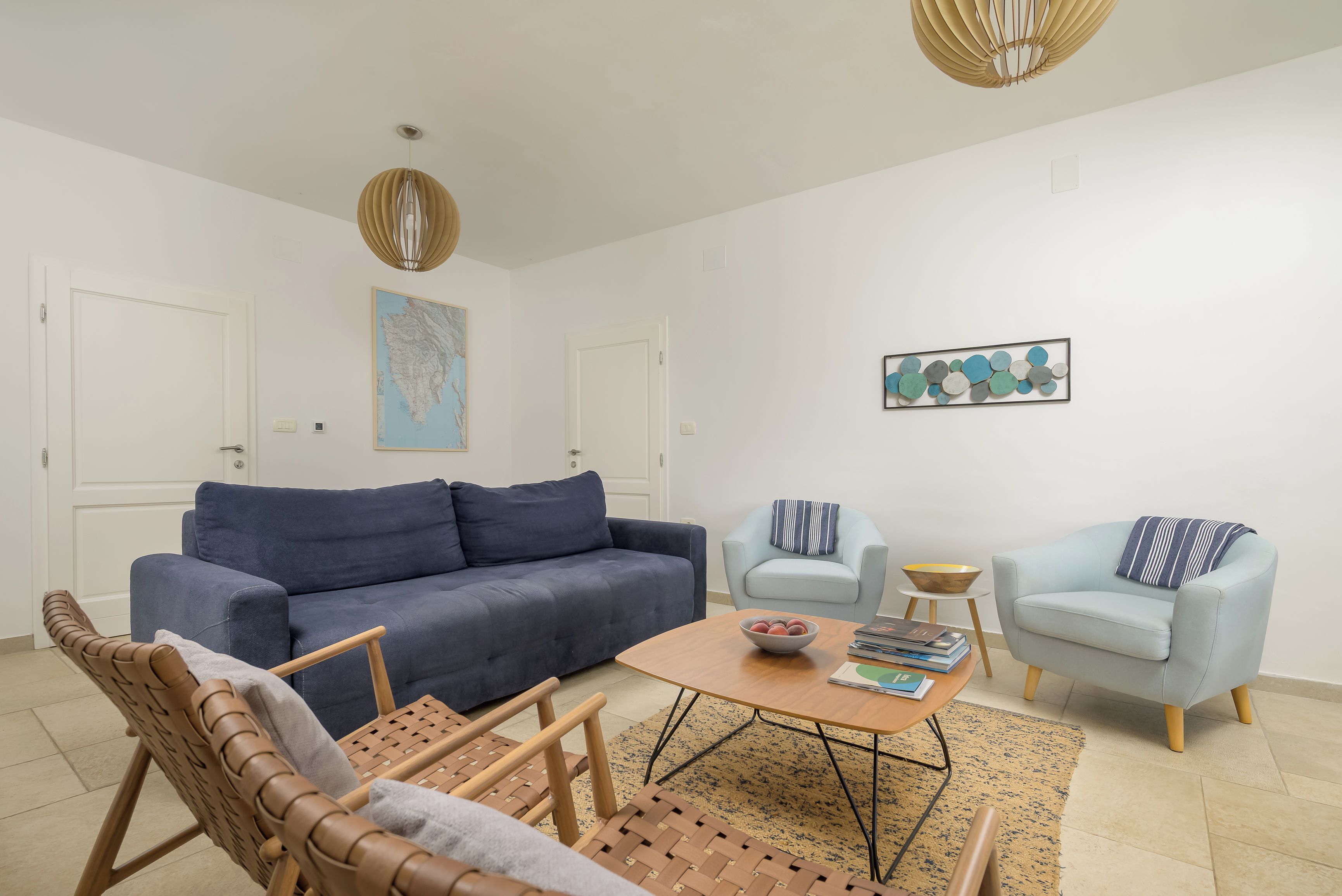 A modern living room with a blue sofa, two armchairs, a coffee table, and a map on the wall.