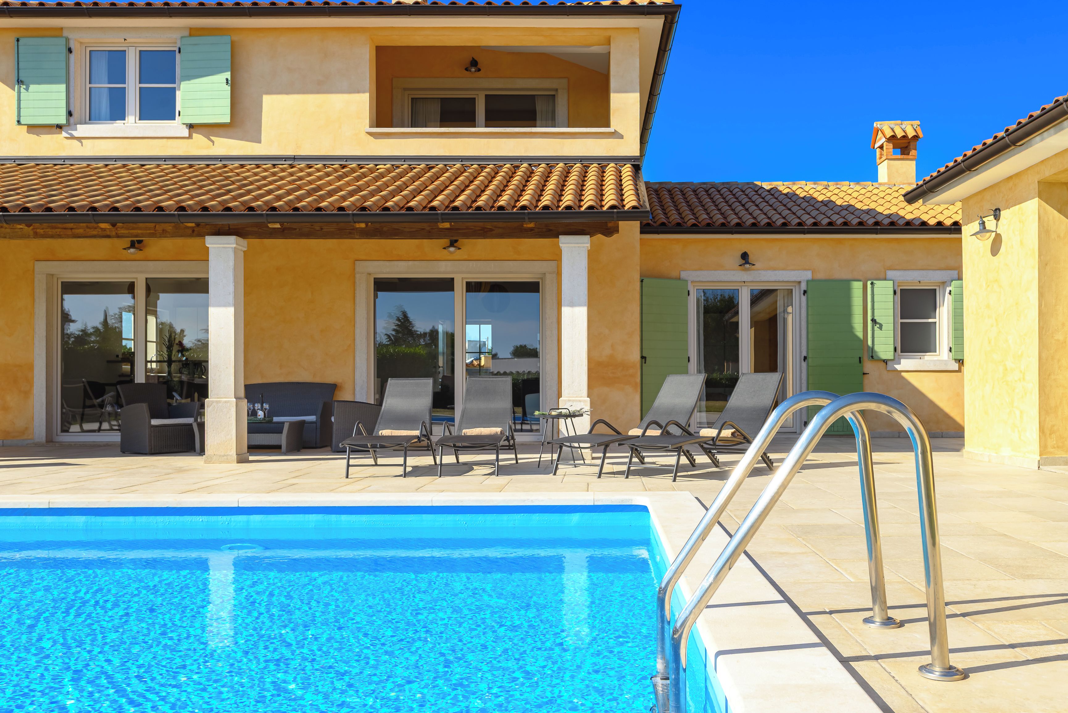 A two-story building with a swimming pool, outdoor seating, and a tiled roof.