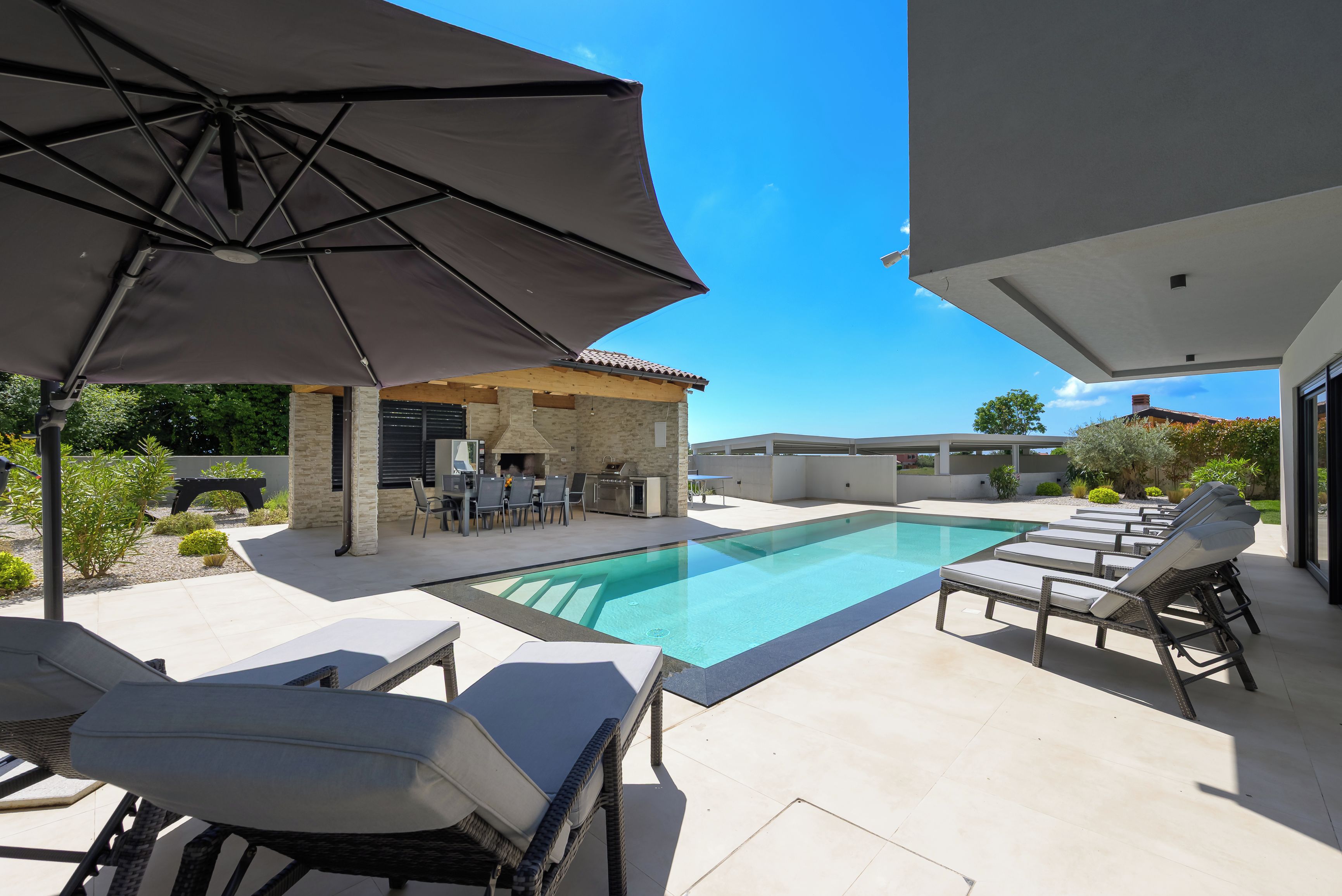 A swimming pool area with lounge chairs, a barbecue setup, and a covered patio.