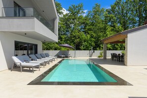 Un área de piscina exterior moderna con sillones de descanso y una zona de estar cubierta.