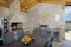 Eine Außenküche mit einer Steinwand, einem Grill, einem Herd und einem Tisch mit Obst.