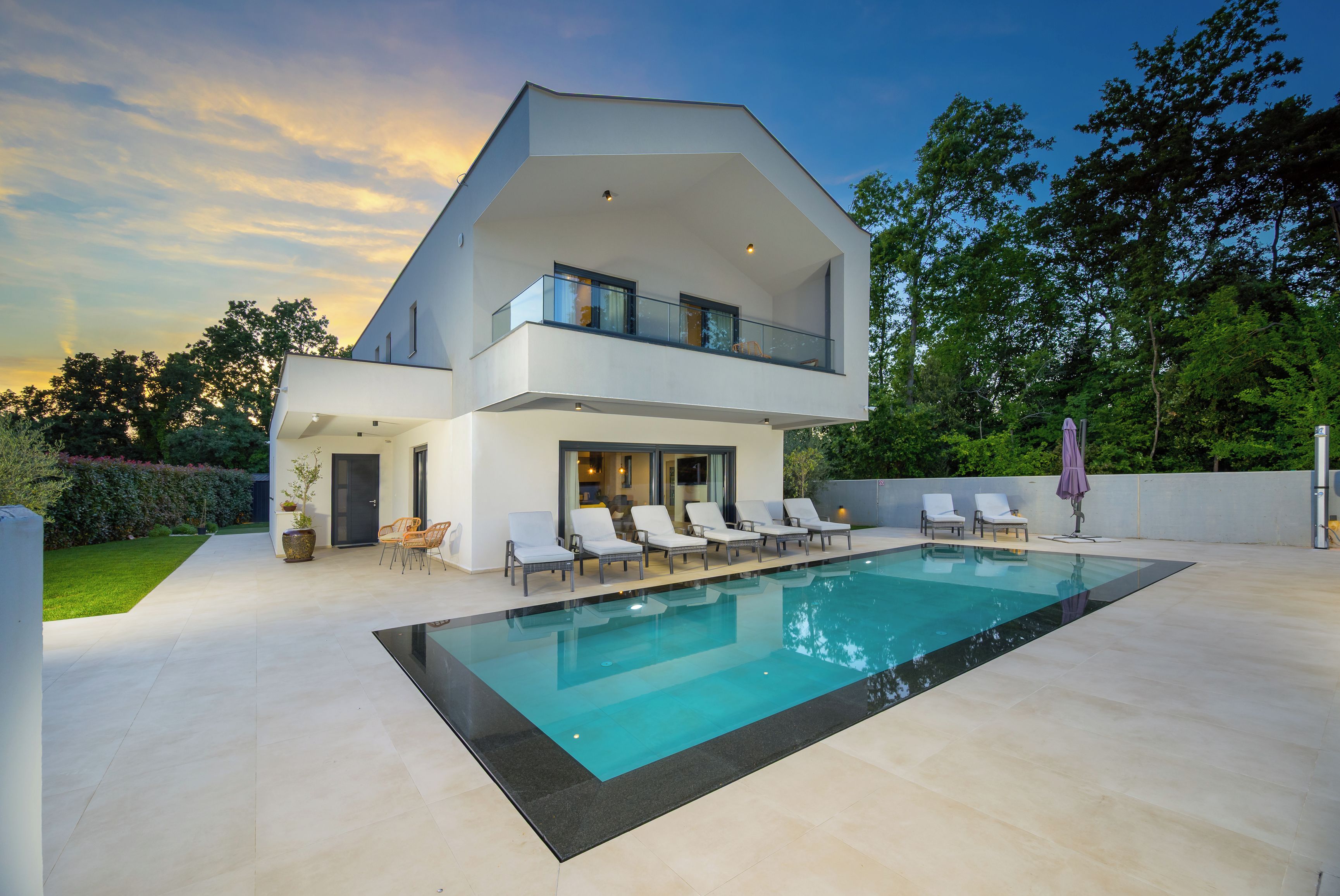 A modern two-story house with a swimming pool, outdoor seating, and a garden.