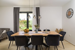 Ein stilvoller Essbereich mit Holztisch, schwarzen Stühlen, Obstschale, Blumenvase und Wanduhr.
