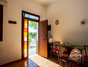 A dining area with a wooden table and chairs, a microwave, and a view of the outside. - Cave Retreat for 3 Guests (Artenara)