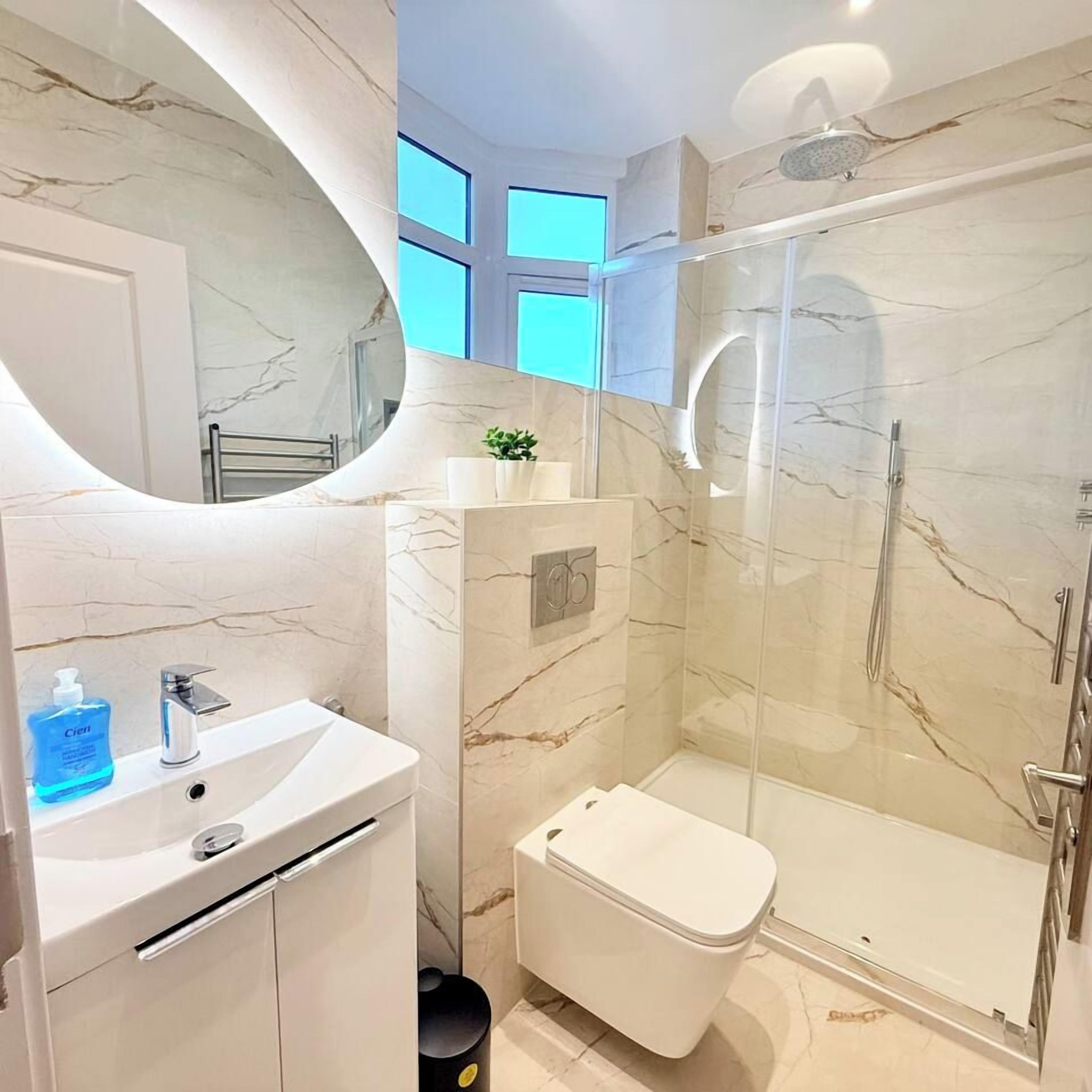 Un baño moderno con tocador de mármol, inodoro y cabina de ducha con mampara de vidrio.
