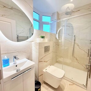A modern bathroom with a marble vanity, a toilet, and a glass-enclosed shower. - Chic London Escape | 5 Min Walk to Tube (Greater London)