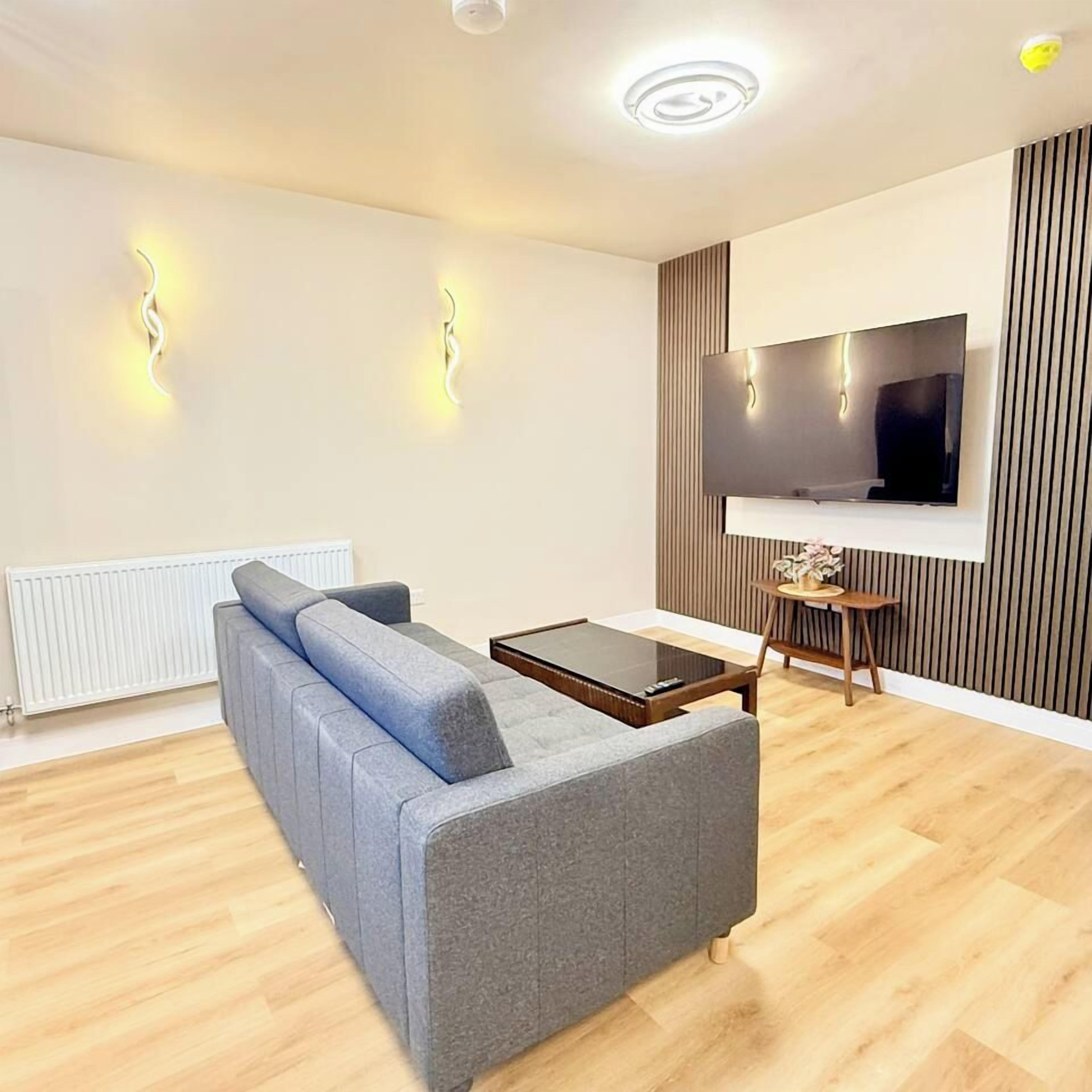 Un salon moderne avec un canapé gris, une table basse, un téléviseur fixé au mur et un radiateur.