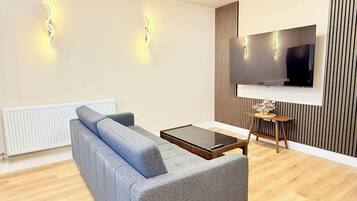 Una sala de estar moderna con un sofá gris, una mesa de centro, un televisor montado en la pared y un radiador.