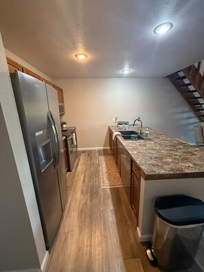 A compact kitchen with a refrigerator, oven, sink, and wooden cabinets. - 3-bedroom condo in perfect Lake Ozark with cool AC and a Pool (Lake Ozark)