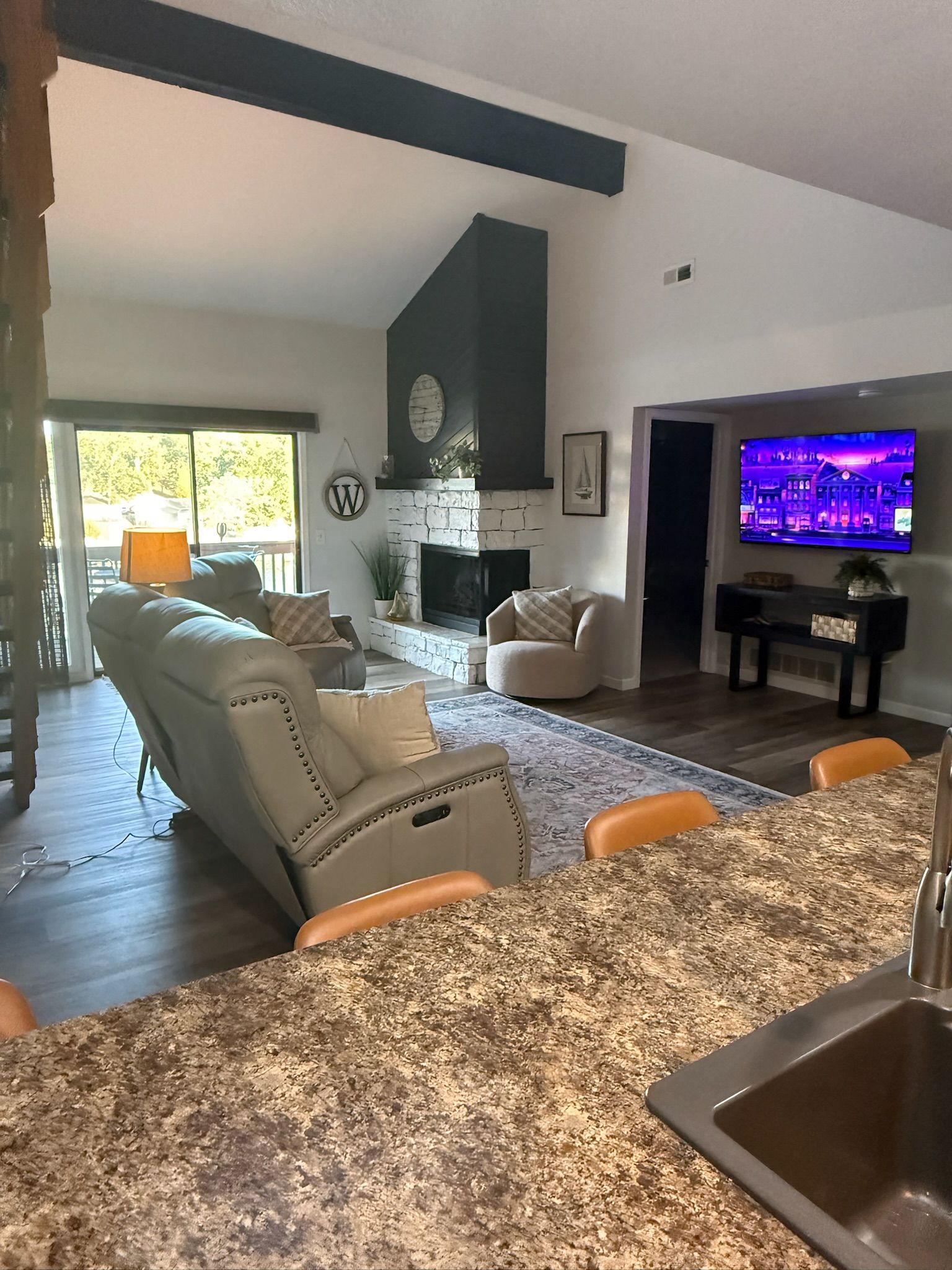 A modern living room with a stone fireplace, a television, and a dining area with a granite countertop.