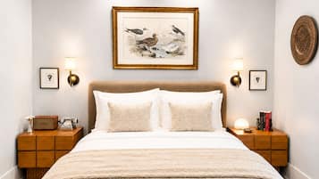 Un dormitorio con una cama grande, dos mesitas de noche con lámparas, una obra enmarcada sobre la cama y un adorno en la pared.