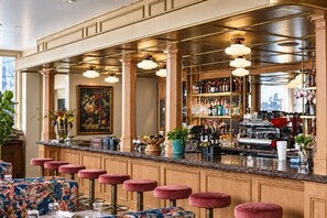 Una zona de bar con mostrador de mármol, varios taburetes, una variedad de botellas y una máquina de café.