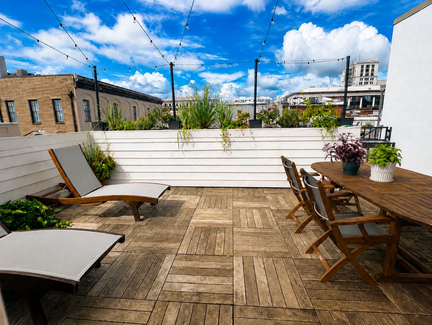 Una terraza en la azotea con suelo de madera, una mesa de comedor con sillas y plantas en macetas.