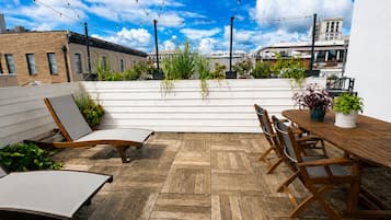 A rooftop patio with wooden flooring, a dining table with chairs, and potted plants.