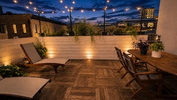 An outdoor patio with wooden flooring, a dining table, chairs, and string lights.