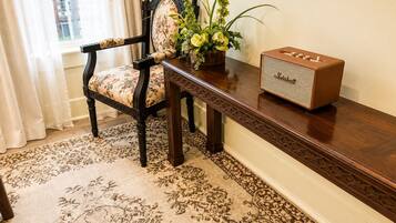 Una habitación con un sillón estampado con motivos florales, una mesita de madera con una radio antigua y una alfombra con estampado.
