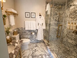 A bathroom with a marble floor, a toilet, a sink, a shower with glass doors, and a robe hanging on a rack.