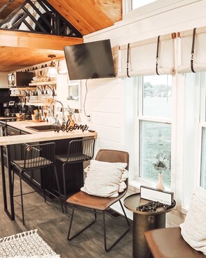 Une cuisine chaleureuse avec un plafond en bois, un téléviseur fixé au mur et une pancarte « Bienvenue » posée sur le comptoir.